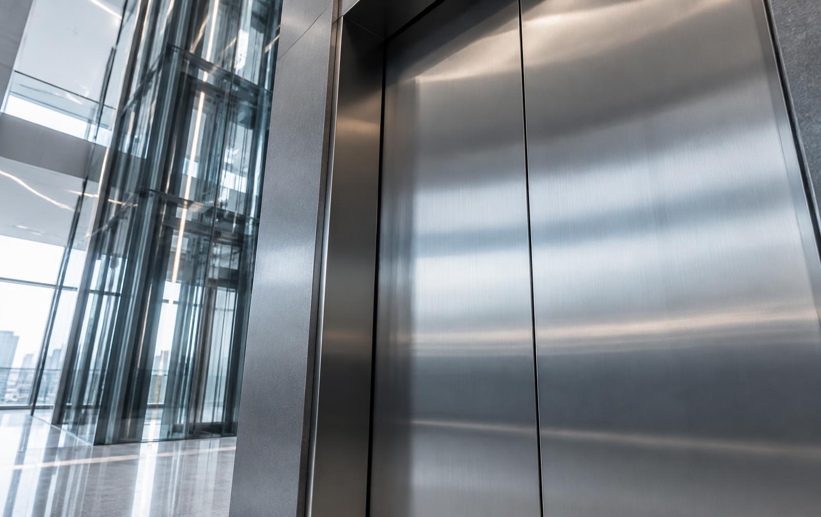 Abstract architectural view of brushed steel lift doors and a glass elevator shaft